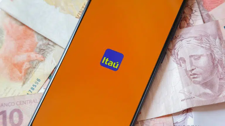 Tela do aplicativo do banco Itaú com notas de Real ao fundo